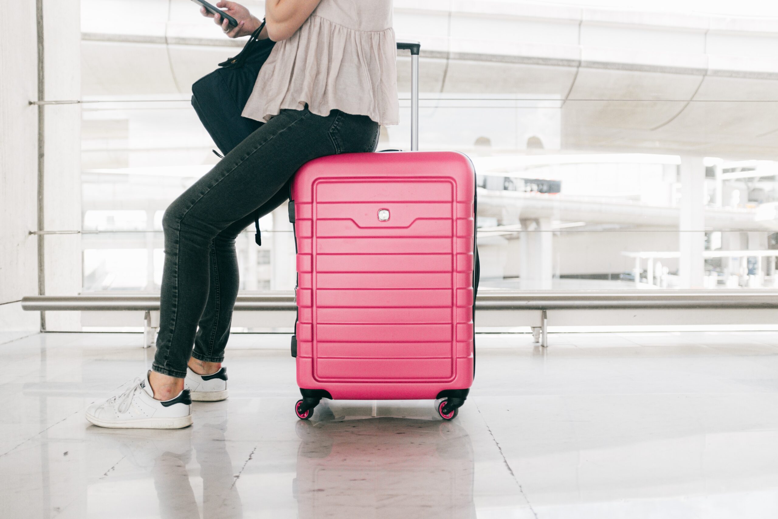 Girl at airport sitting on pink roller luggage.